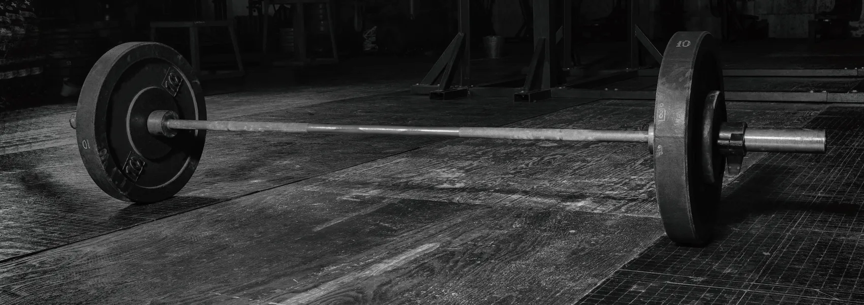 A barbell loaded with weight at each end stands on a gym floor in black and white